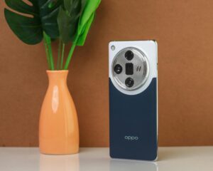 A modern smartphone with a unique camera design displayed next to a vase with green leaves on a brown background.